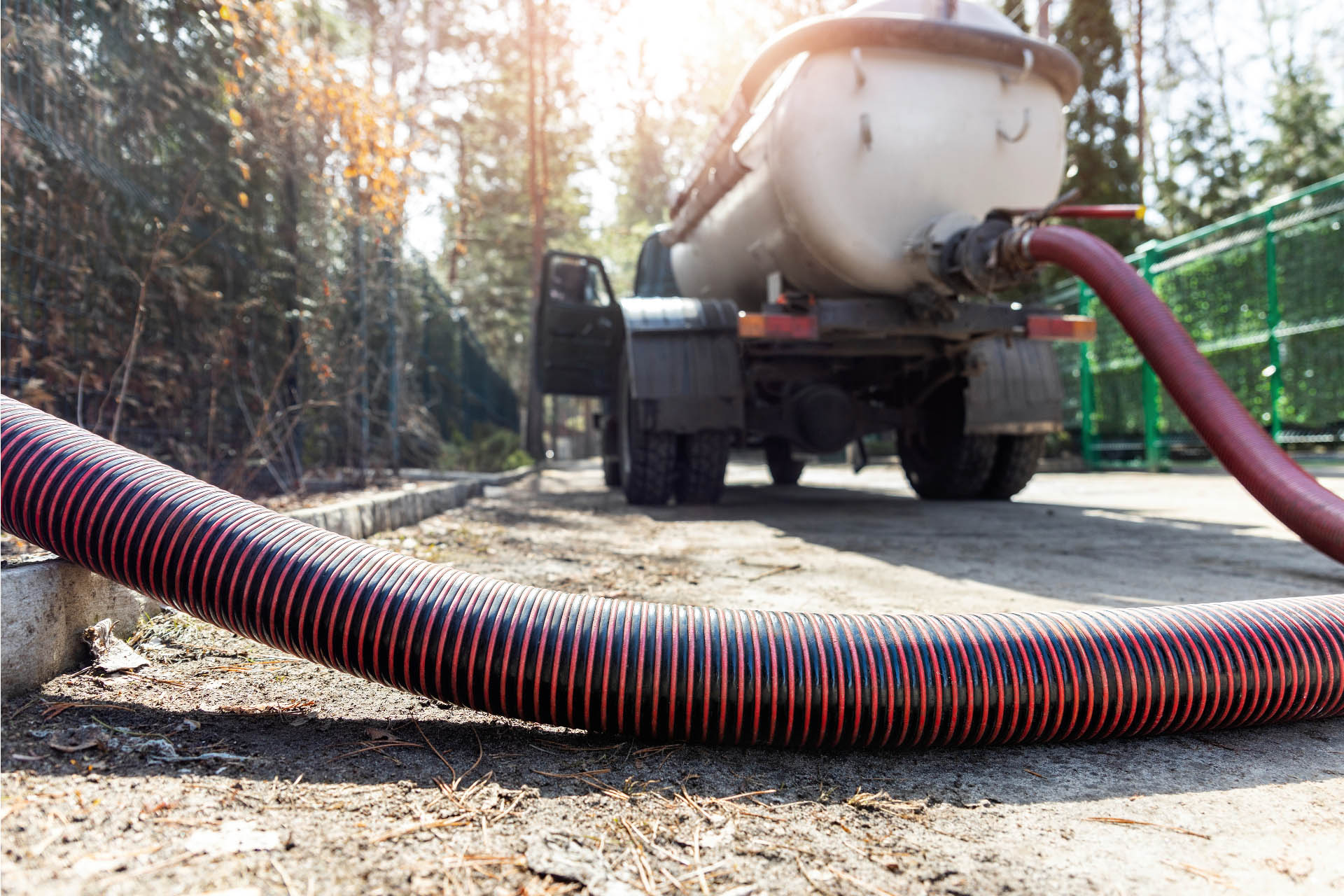 A hose connected to a truck at home on a dirt road provides septic tank pumping services.