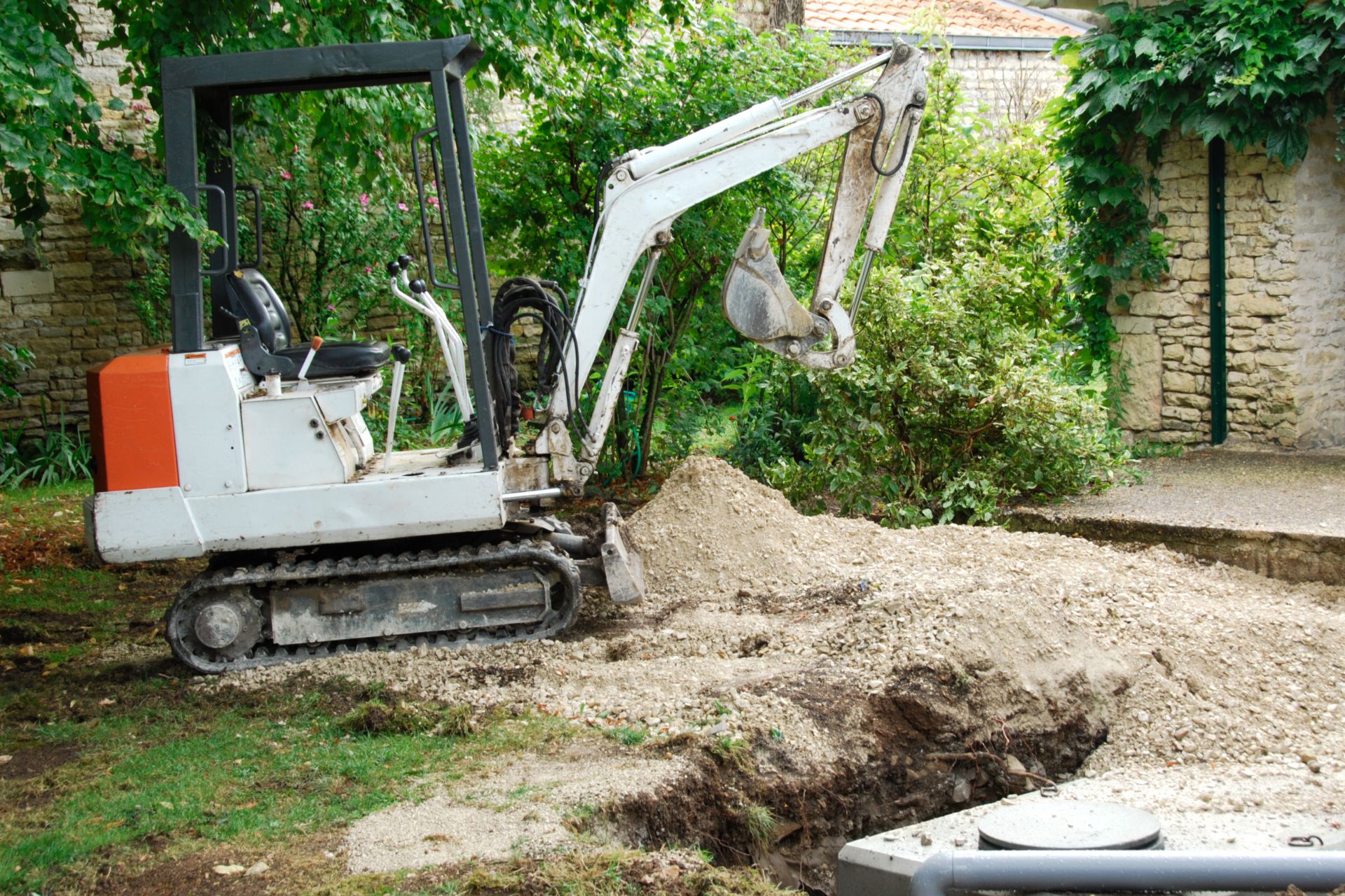 About Us: A small excavator digging a hole in a yard.