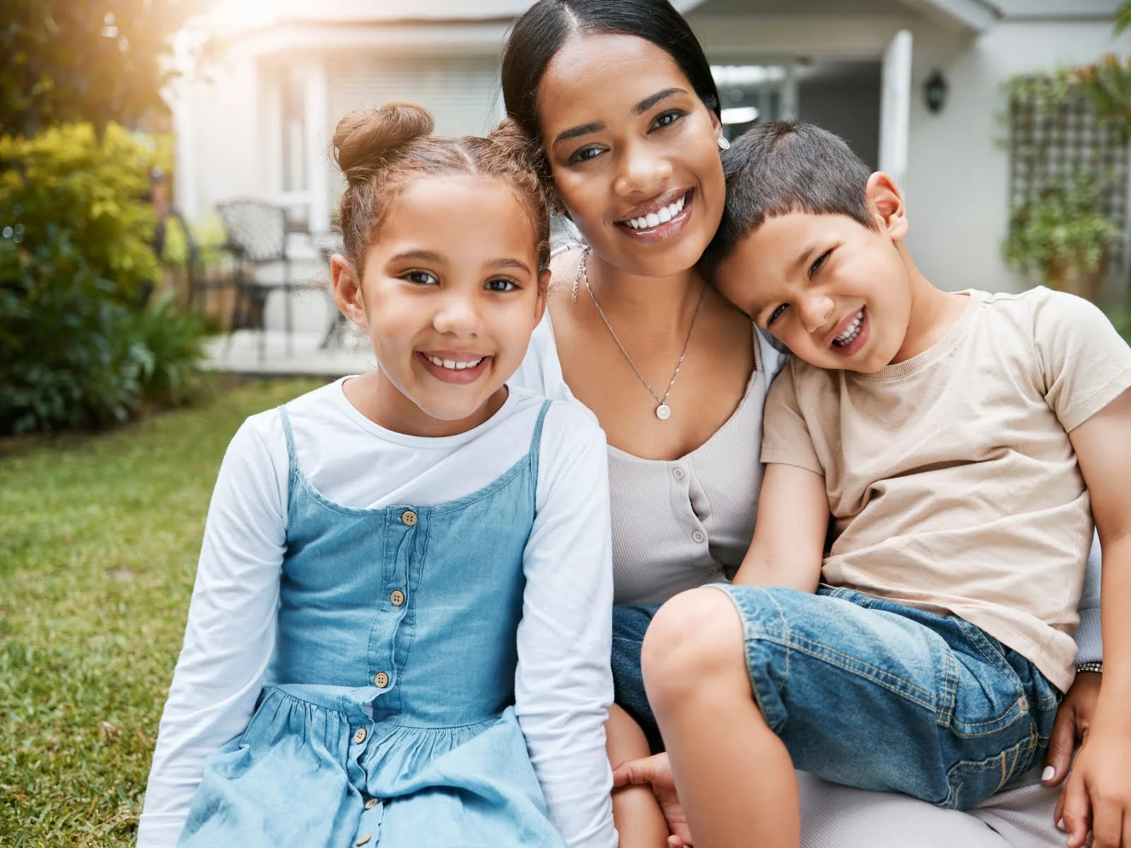 A woman and her children are enjoying a peaceful afternoon on the grass in front of their home.