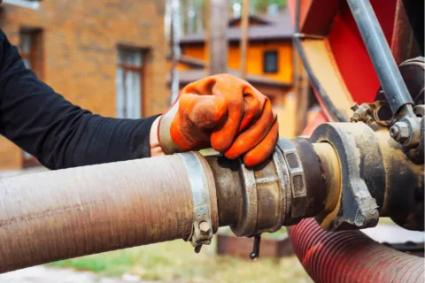A man in orange gloves is diligently working on a pipe as part of septic system care.