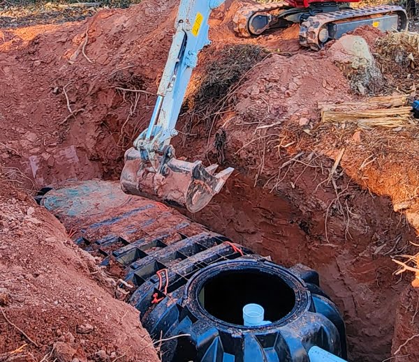 An excavator performing a septic tank installation by digging a hole in the ground.