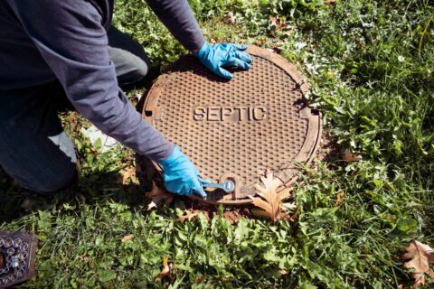 A man is putting an advanced septic systems manhole cover on the ground.