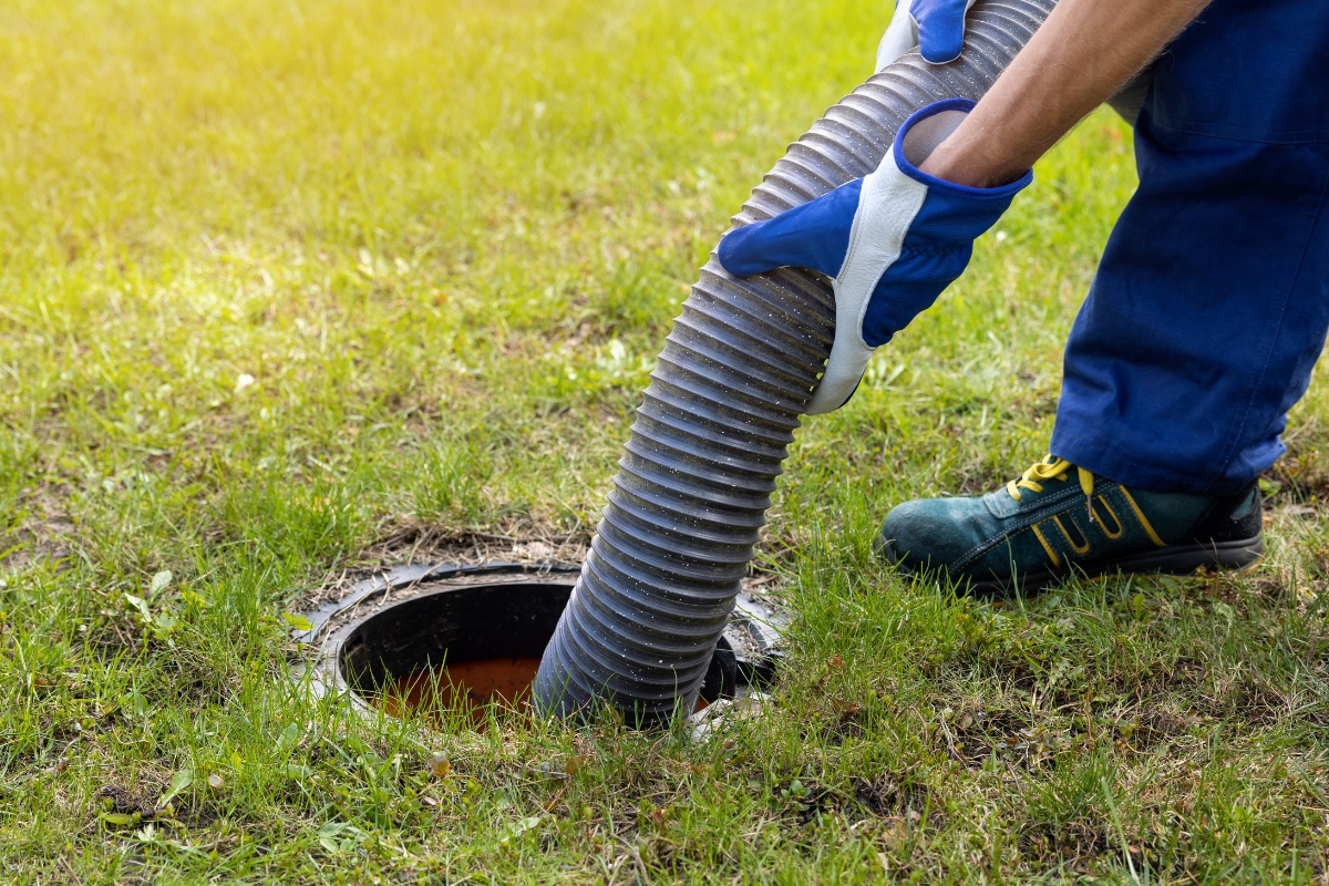 Worker inserting a flexible hose into a septic tank for emergency cleaning or maintenance.