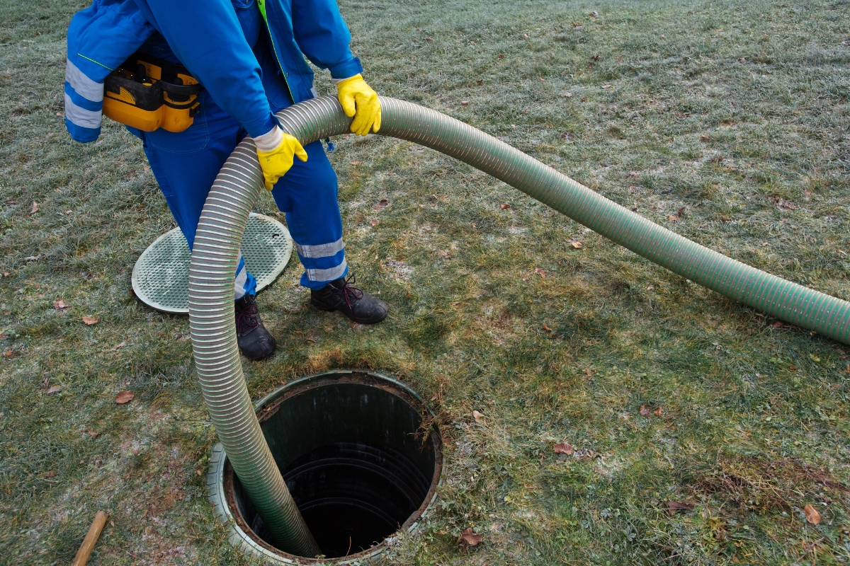 Worker in blue coveralls and yellow gloves inserting a hose into a manhole for emergency septic services maintenance or cleaning.