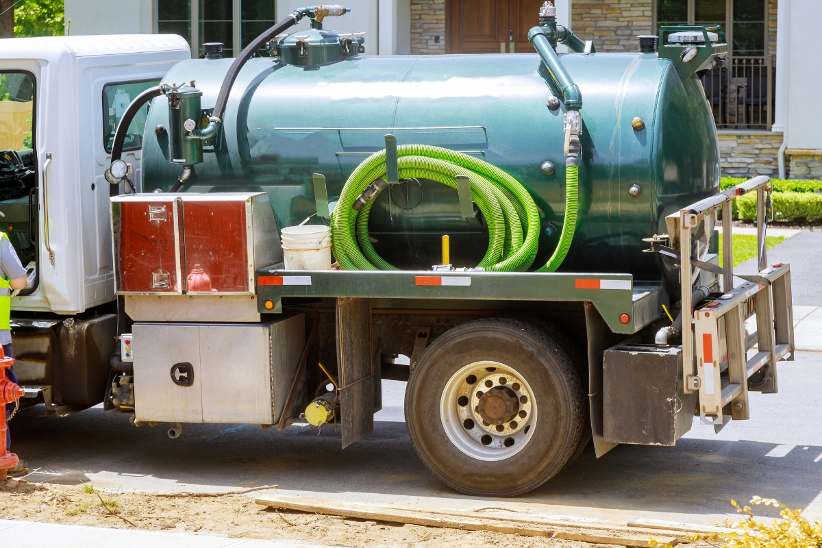 A septic truck equipped with hoses and a storage tank for emergency septic services parked on a residential street.