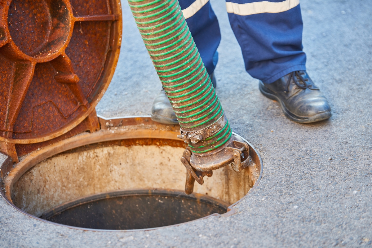 Worker using a hose for emergency septic services near a manhole cover.