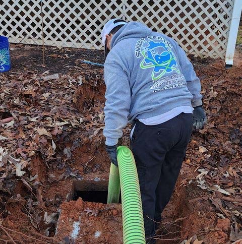 Person installing a drainage pipe outdoors for tank pumping.