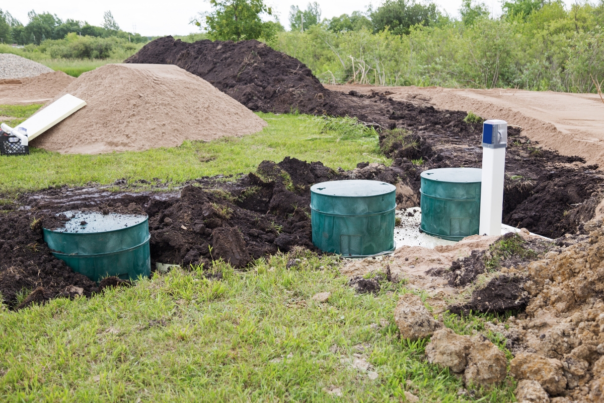 Construction site with soil excavation, green barrels for water conservation, and piles of sand and earth in the background.