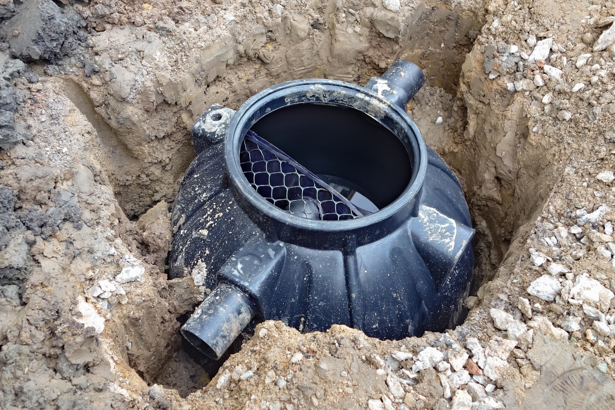 A partially buried black plastic septic tank with two visible pipe connections, installed in a hole amid soil and loose gravel, exemplifies green septic systems by efficiently managing waste while minimizing environmental impact.