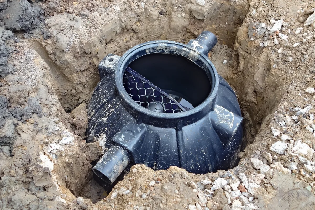 Green Septic Systems: The Future of Eco-Friendly Waste Management 3 A partially buried black plastic septic tank with two visible pipe connections, installed in a hole amid soil and loose gravel, exemplifies green septic systems by efficiently managing waste while minimizing environmental impact.