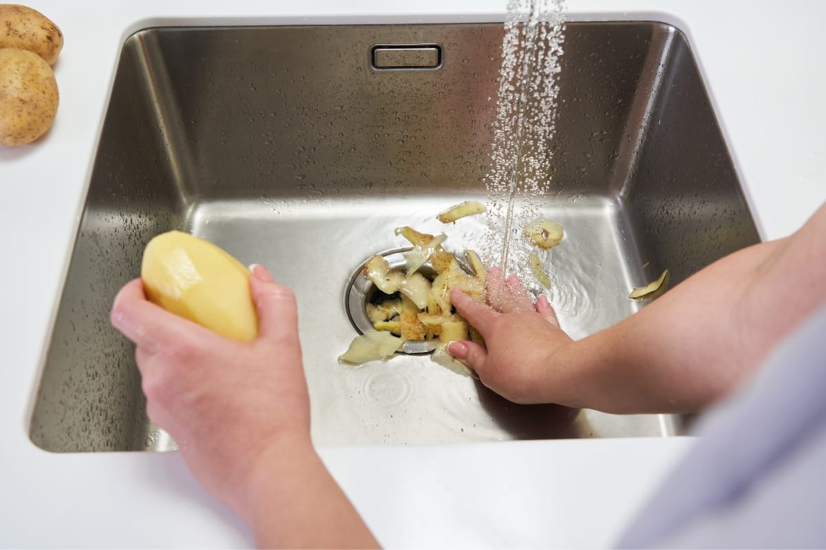 A person is peeling potatoes over a sink with running water, with potato peels collecting in the basin—a scene commonly encountered during home renovation projects.