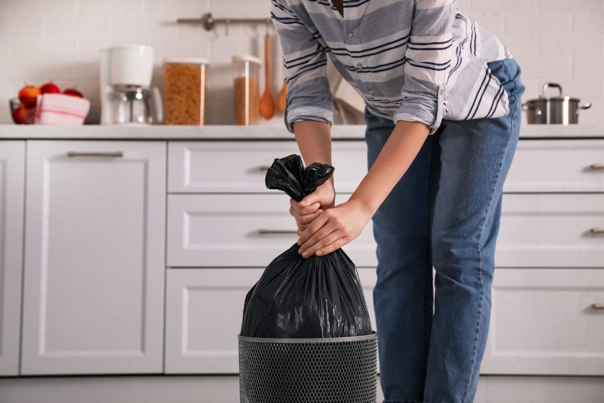 Person in a striped shirt and jeans tying a black garbage bag in a modern kitchen, likely tidying up after a home renovation.