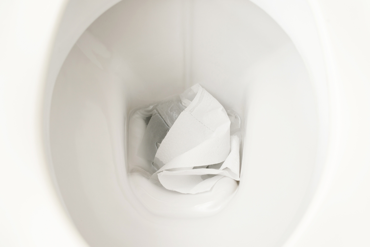 A close-up of a white ceramic toilet bowl with used toilet paper inside, highlighting the importance of regular septic tank cleaning.