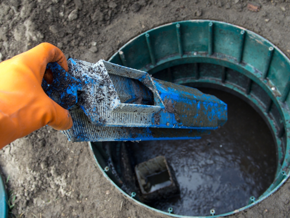 A gloved hand holds a blue, dirty tool over an open green cylindrical container filled with murky water, as part of professional inspection services.