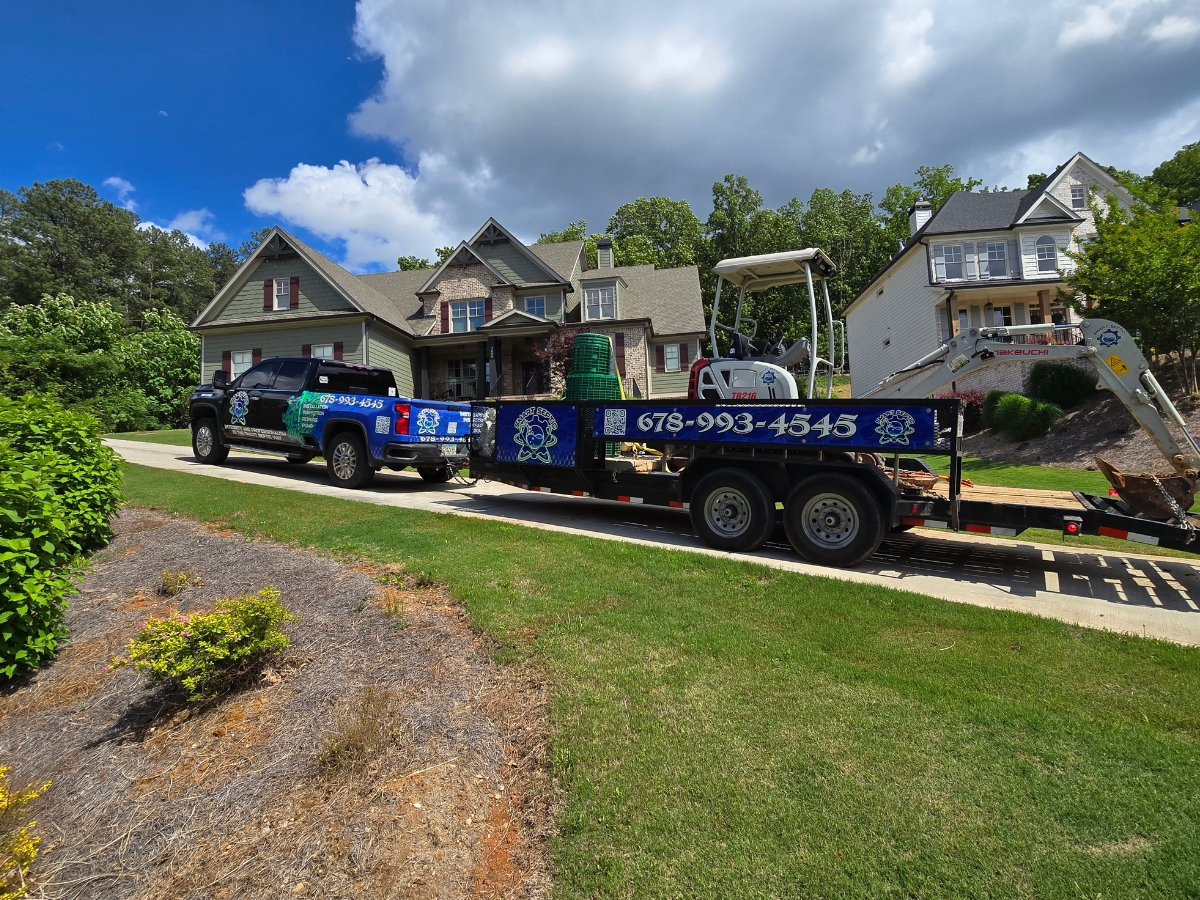 A pickup truck towing a trailer with landscaping equipment is parked in front of a suburban house on a sunny day, where Professional Septic Inspection and Repair services are also being conducted.