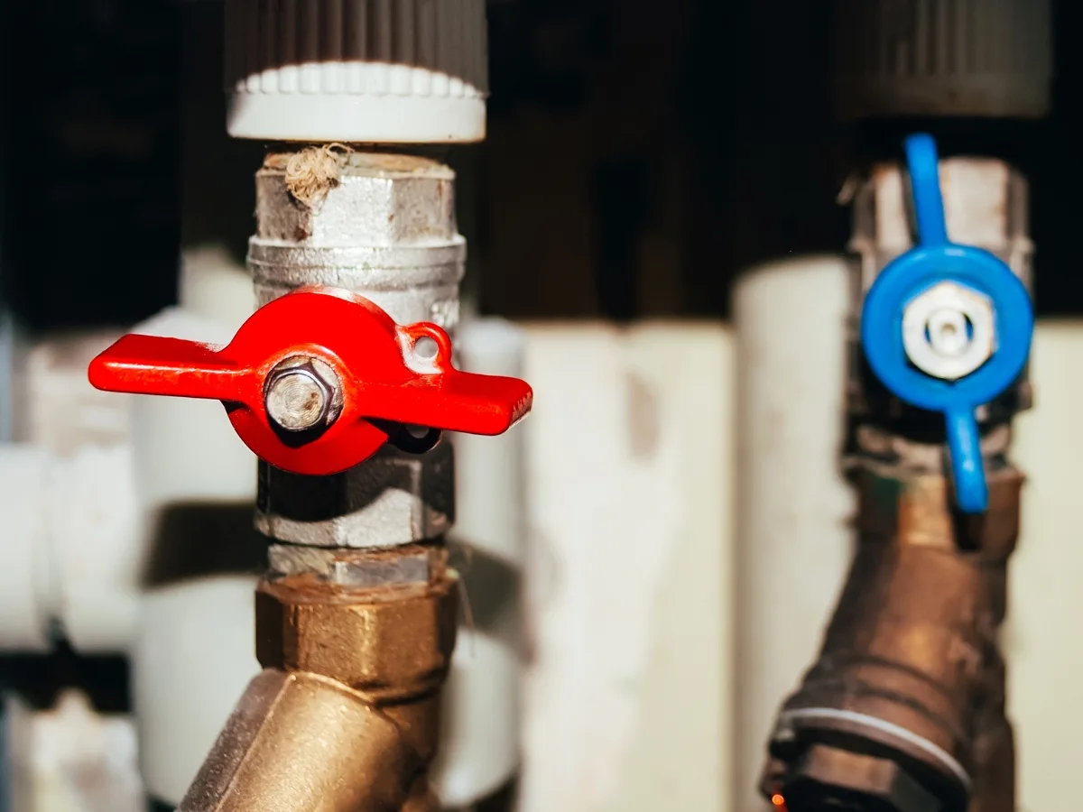Close-up of two pipe valves, one with a red handle and the other with a blue handle, attached to metal pipes, crucial for emergency septic tank cleaning.