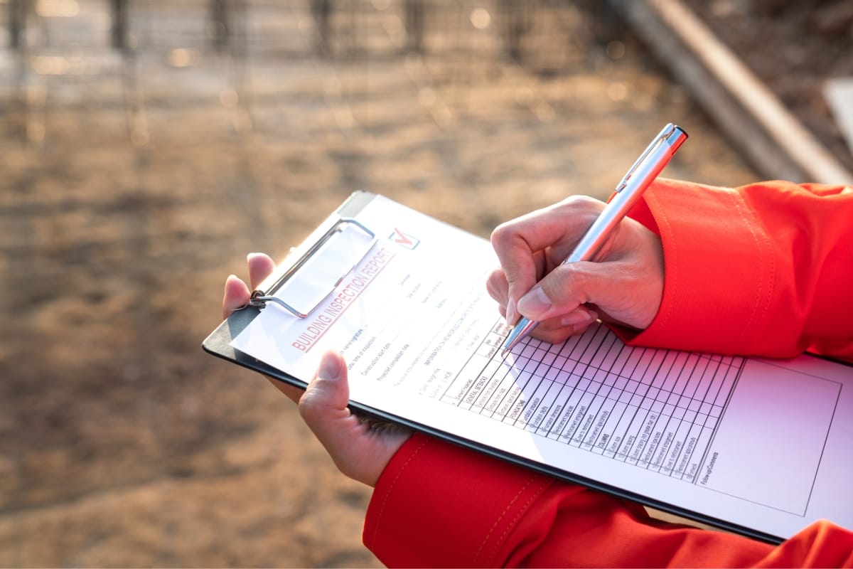 Person in an orange jacket fills out a checklist on a clipboard outdoors, ensuring everything is in place for the aerobic septic system inspection.