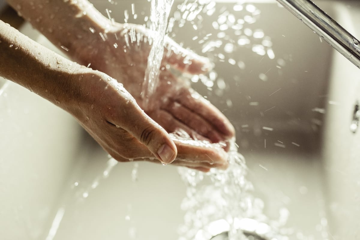 Hands being washed under running water in a kitchen sink, ensuring cleanliness. Just as you maintain hygiene here, it's essential to consult expert tips on how often you should pump your septic tank for a well-functioning home system.