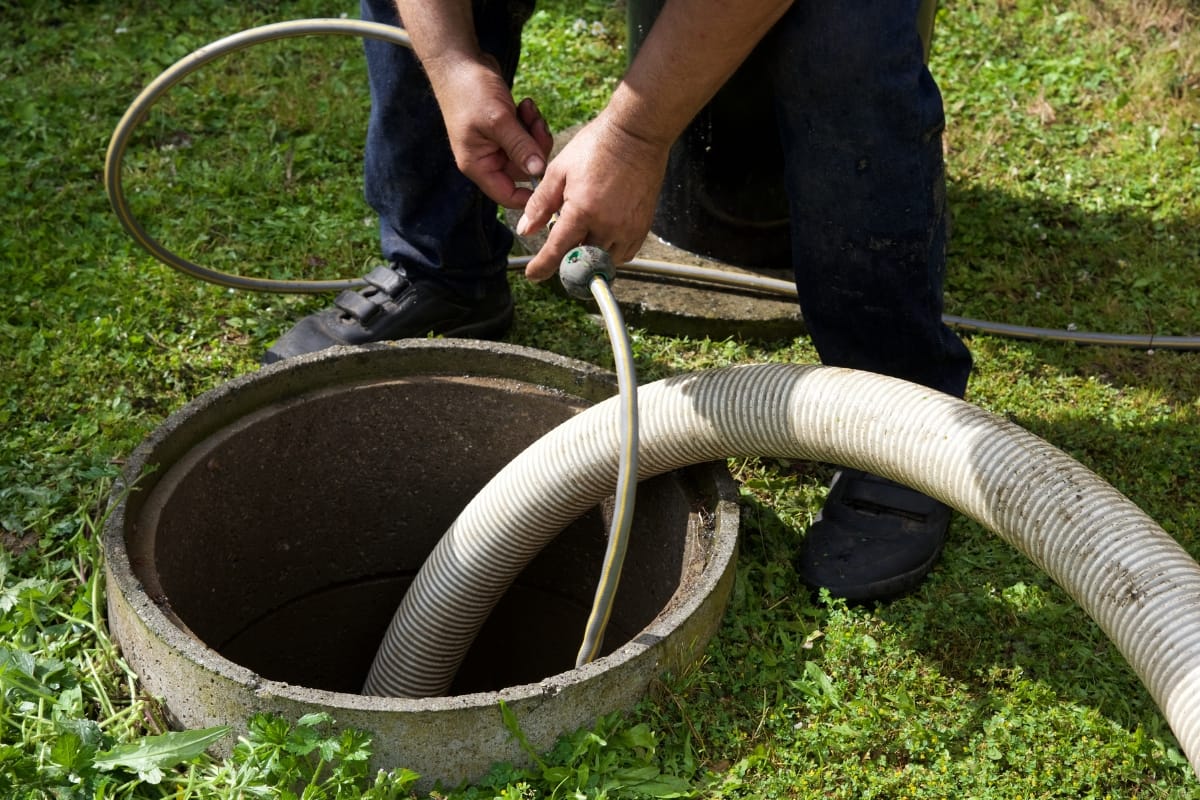 A person expertly manages a hose connected to a round concrete septic tank on lush grass. Curious about maintenance? Discover how often you should pump your septic tank with expert tips to ensure optimal performance and longevity.