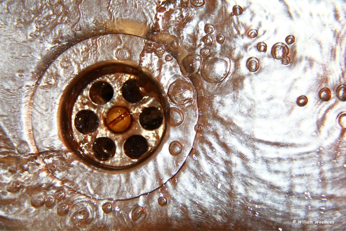 Close-up of a drain with flowing water and bubbles around it. The metal surface is visible, creating a swirling pattern in the water—much like the signs you might see when figuring out how to know if your septic tank is full.