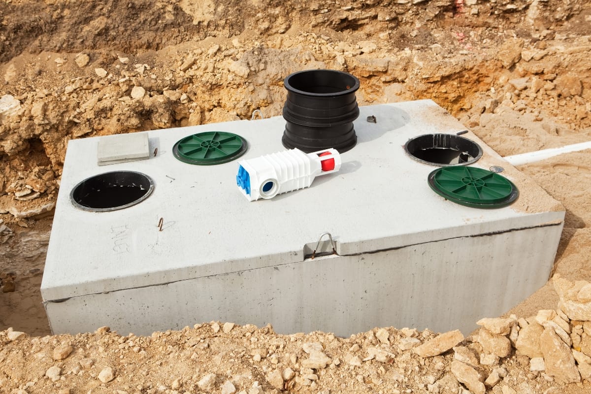 Partially buried in the ground, this concrete septic tank showcases circular green and black covers with pipes on top. Unlike mound septic systems, this conventional setup is designed for effective wastewater management.