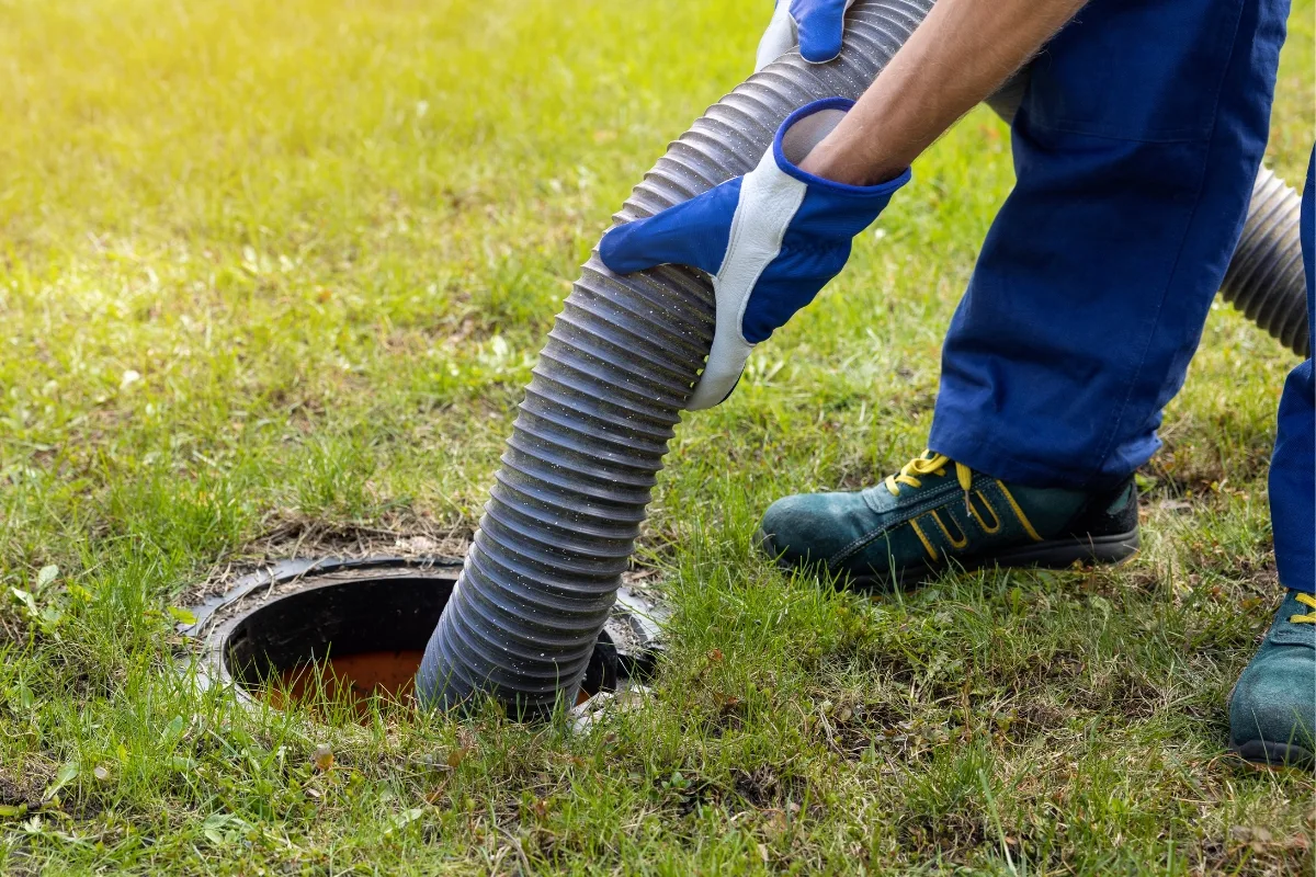 Essential Guide to Effective Residential Septic Tank Maintenance Strategies 7 A person in gloves and protective clothing manages a hose, carefully inserting it into a ground opening on a grass surface, as part of routine residential septic tank maintenance.