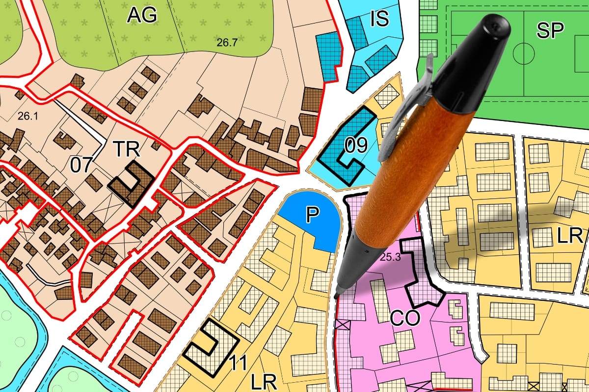 A map with various colored zones, labeled areas like AG, CO, and LR, features buildings and roads. A pen points to a spot in a pink zone marked "CO," highlighting specific septic drain field requirements for the area.