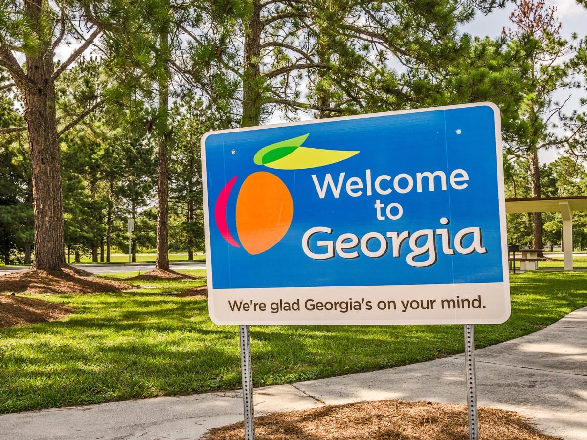 A sign reads "Welcome to Georgia" with an orange icon, under a blue sky and surrounded by trees, reminding visitors of the state's charm and its practicalities, like understanding septic inspection requirements for smooth transitions into Georgia living.