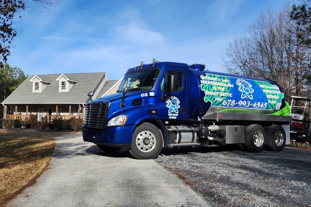 A blue septic service truck, belonging to the best septic company in town, is parked in the driveway of a suburban house with a lush lawn and trees in the background.