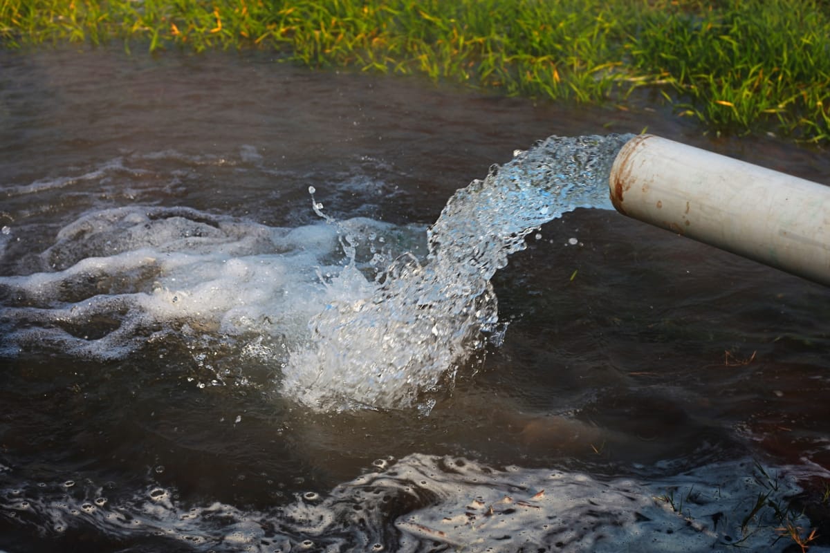 A pipe releases water into a grassy area, tapping into the groundwater and creating a small pool with bubbles and ripples in the water.