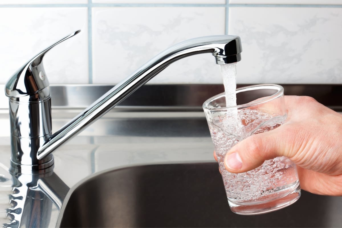 A hand holds a glass under a running faucet, filling it with refreshing groundwater in a kitchen sink.