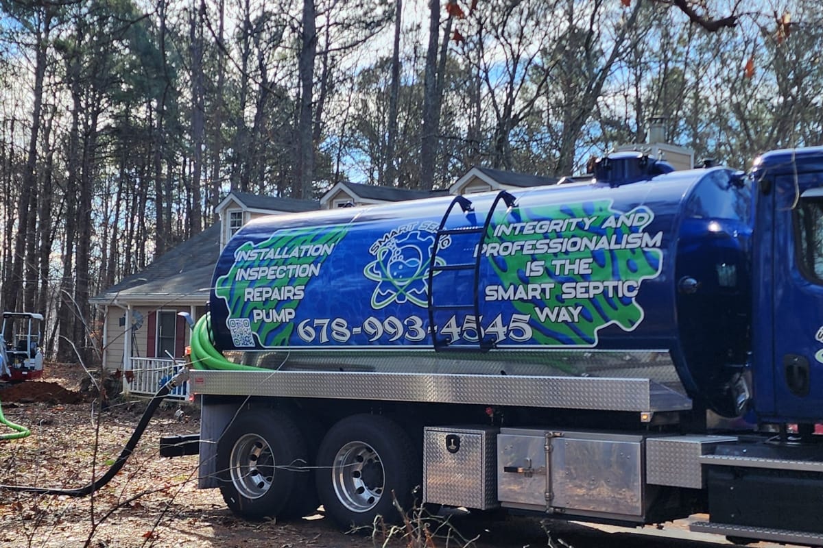 A local septic services truck is parked outdoors, showcasing its installation, inspection, and repair services with a focus on integrity and professionalism. Local septic tank installers ensure quality service. A house and trees provide a picturesque backdrop.