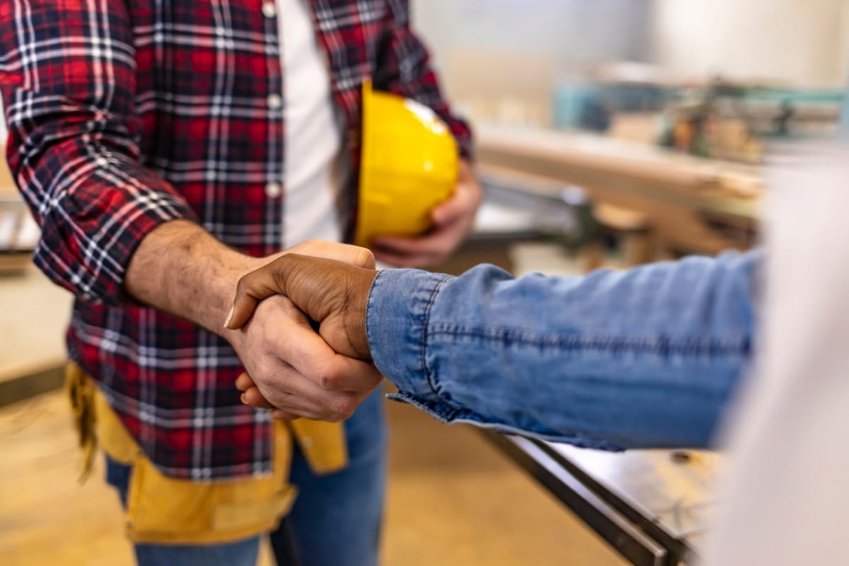 Two people shaking hands, sealing the deal with a nod of trust; one holds a yellow hard hat, embodying the expertise of local septic tank installers.