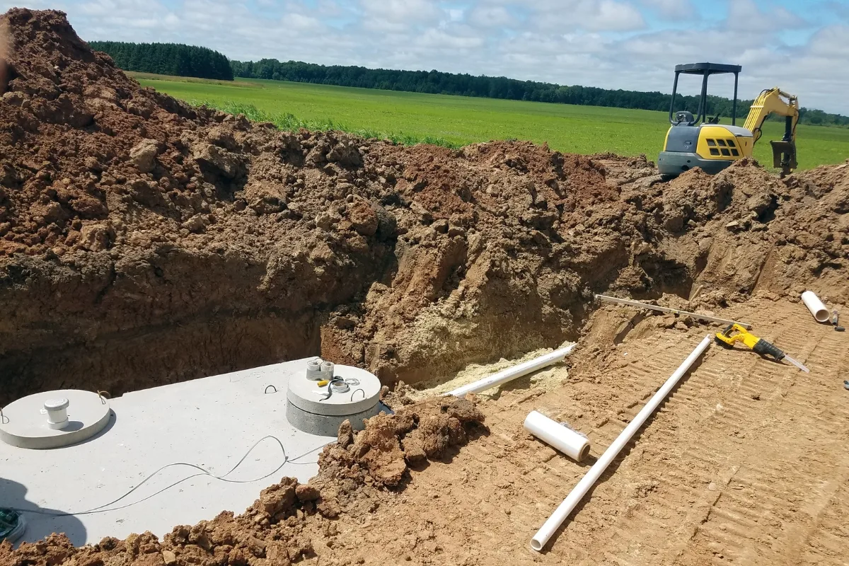 Strategies for Septic Systems to Lower Nitrogen Pollution 2 Excavated site in a field reveals a concrete tank partially buried amidst construction equipment and PVC pipes laid out, as efforts to curb nitrogen pollution intensify.