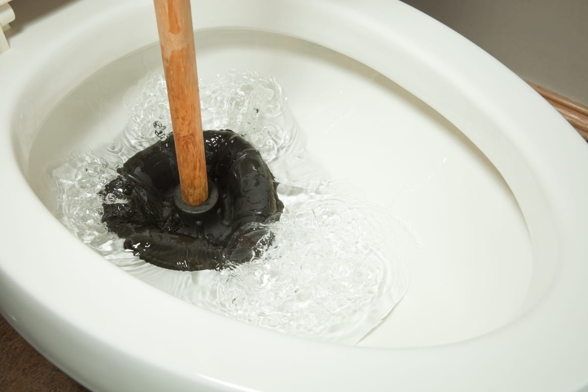 A toilet being unclogged with a plunger, causing water to splash—a common scenario in septic emergencies.