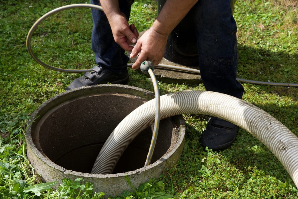 The person is performing a septic system inspection, expertly maneuvering hoses at an open tank on the lawn.