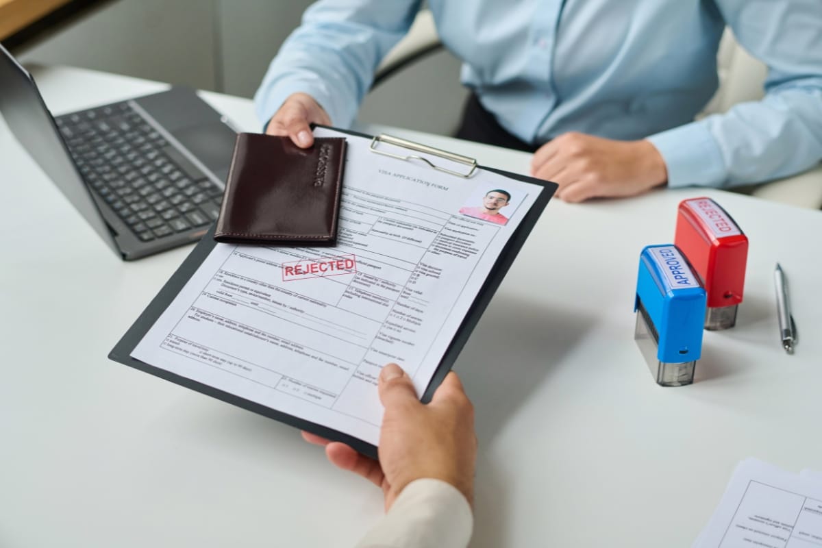 A clipboard with a rejected application form is handed over, while two stamps labeled "Rejected" and "Approved" lie prominently on the desk, suggesting a rigorous site assessment process.