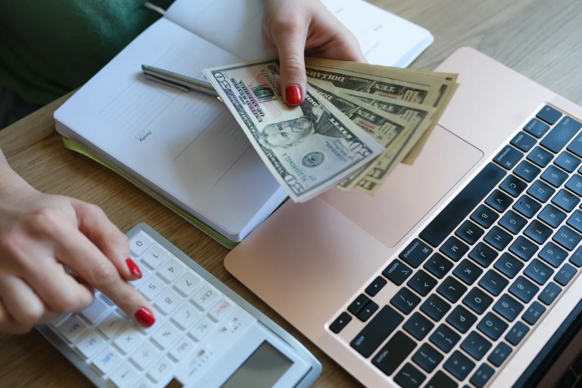 How Much Does a Septic Tank Cost? Factors Affecting Prices 1 A person uses a calculator while holding U.S. dollar bills, likely budgeting for expenses like septic tank cost, near a laptop and an open notebook on a desk.
