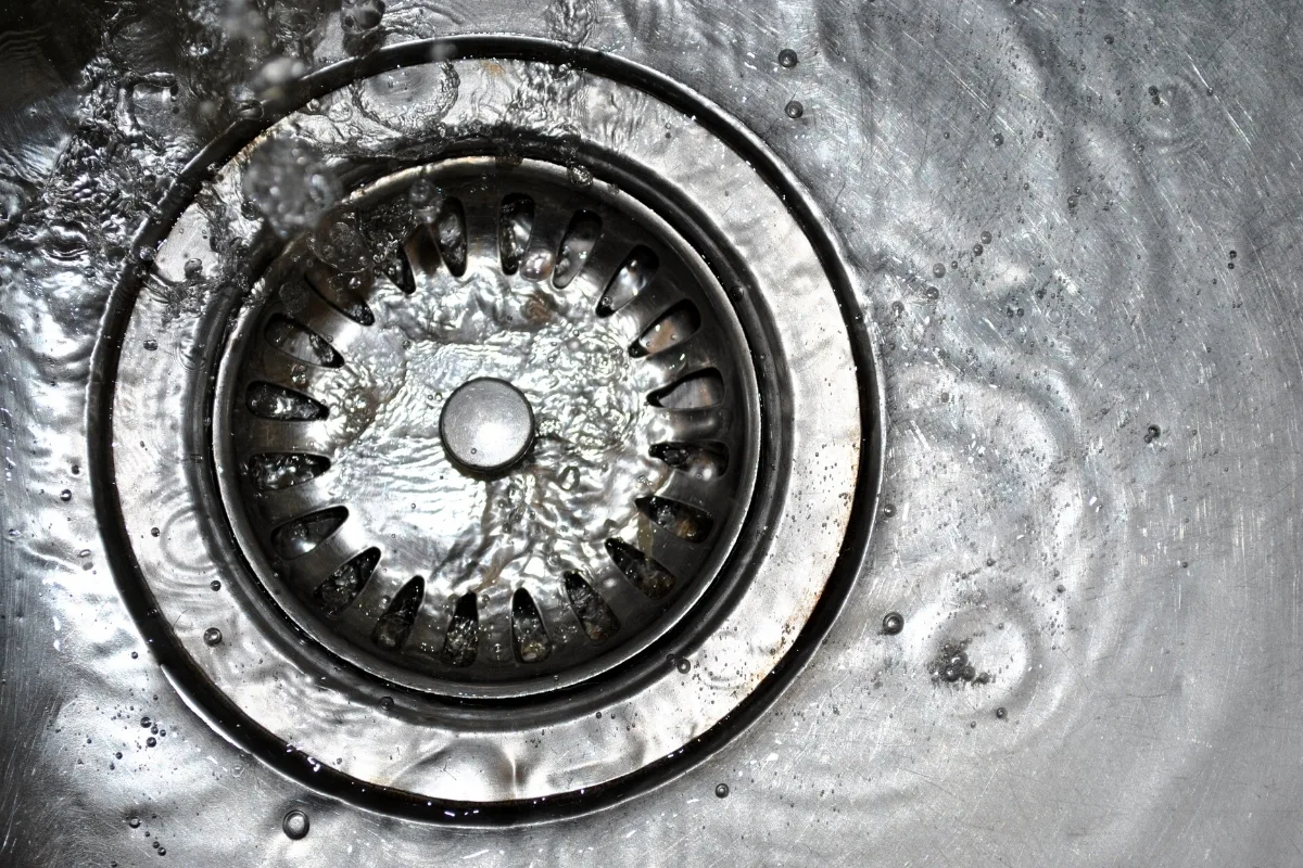 Warning Signs Your Septic Tank Needs Pumping 4 Close-up of a stainless steel sink drain with water swirling around it, hinting at signs your septic tank needs pumping.
