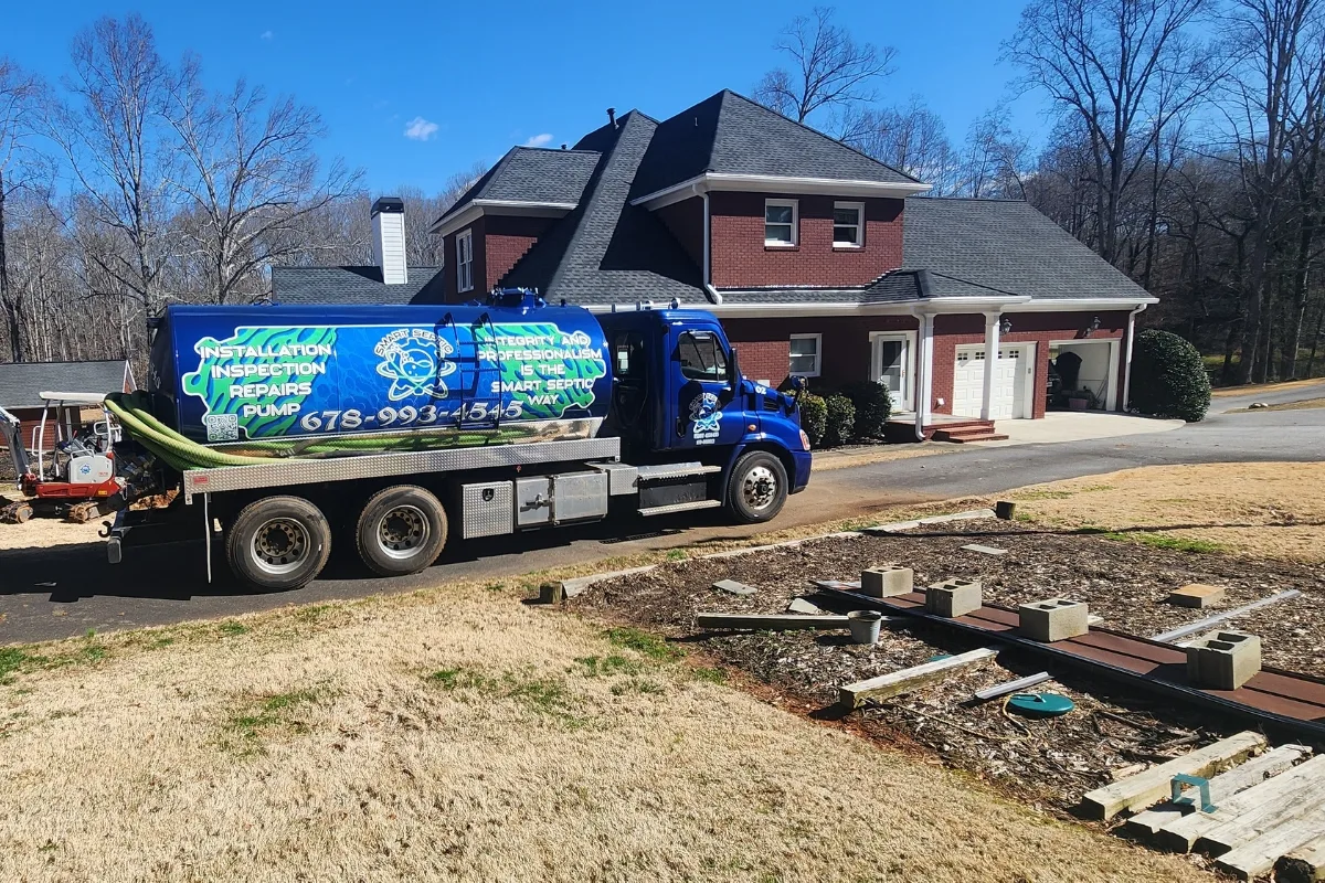 DIY Septic System Maintenance Georgia: Essential Tips for Homeowners 4 A blue septic service truck is parked in front of a large red brick house with a paved driveway, surrounded by visible yard work equipment designed for longevity.