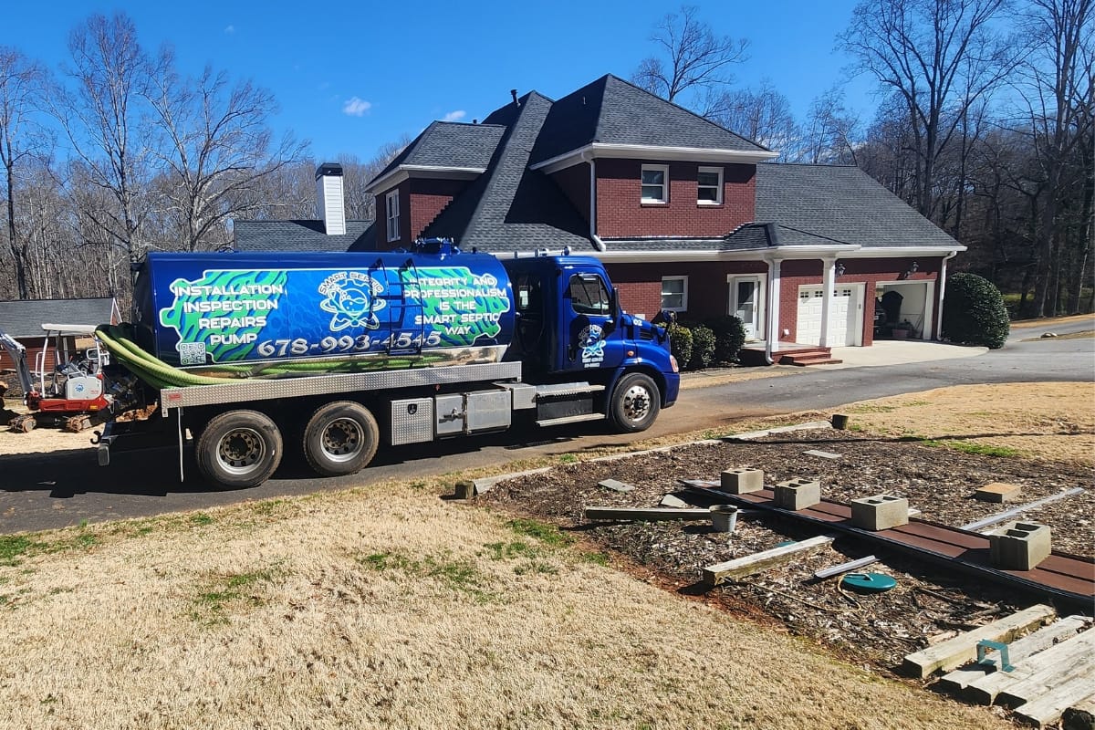 A septic service truck, following septic system repair guidelines, is parked in front of a red brick house on a sunny day.