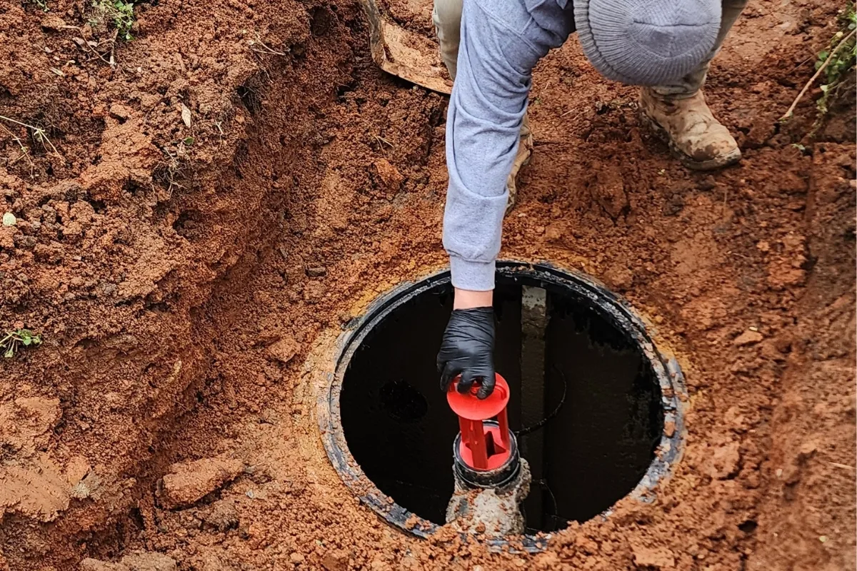 DIY Septic System Maintenance Georgia: Essential Tips for Homeowners 5 A person wearing gloves and a beanie expertly installs a valve in an underground pipe within the dug-out soil area, part of the meticulous process involved in septic tank inspections in Smyrna.
