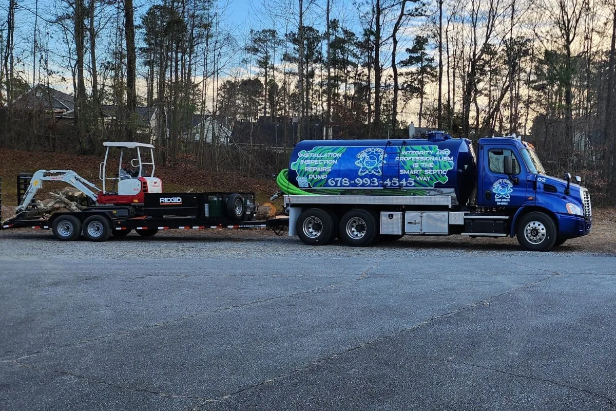 Georgia Septic System Regulations: A Guide for Homeowners 4 A blue septic service truck, proudly bearing its Metasync logo, is parked on a paved area. It tows a trailer loaded with excavation equipment. In the background, trees and houses complete the scene with a serene touch.