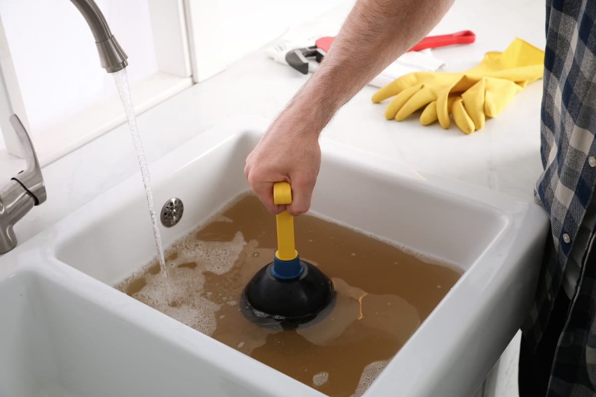 Buying a Home with a Septic System in Acworth, GA: Essential Insights 3 A person uses a plunger to unclog a sink filled with dirty water; for those buying a home with a septic system, keeping tools and yellow gloves nearby is essential for routine maintenance.