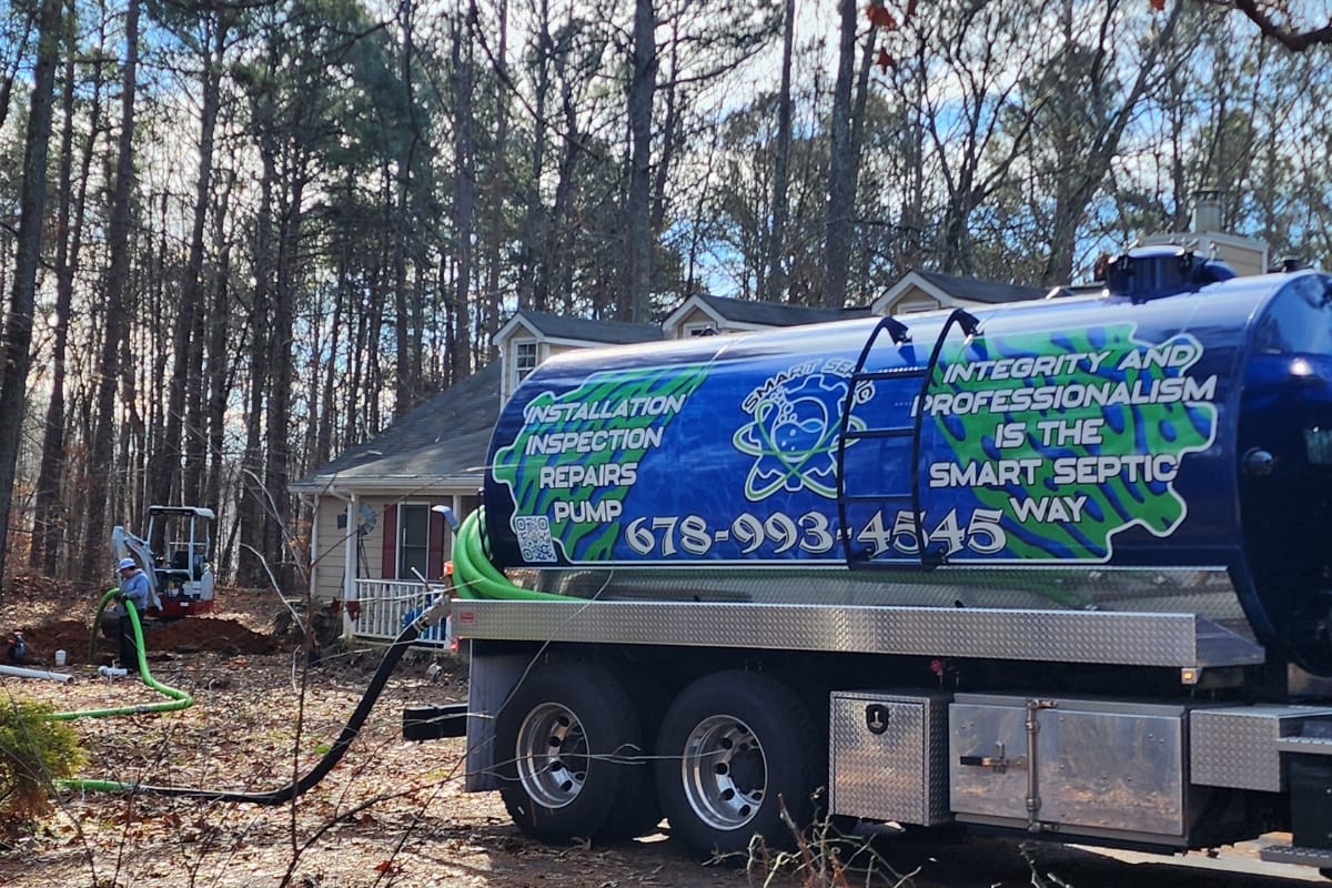 Buying a Home with a Septic System in Acworth, GA: Essential Insights 4 A septic service truck is parked in front of a house in a wooded area, with hoses connected to perform maintenance—an important step when buying a home with a septic system.