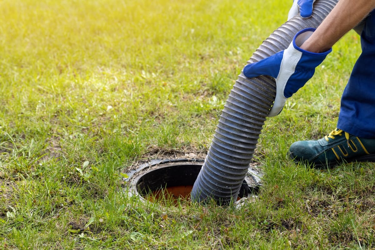 Buying a Home with a Septic System in Acworth, GA: Essential Insights 7 A person wearing gloves inserts a large hose into an outdoor septic tank opening on a grassy lawn—an important maintenance step when buying a home with a septic system.