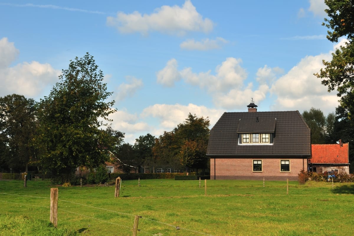 Off-Grid Septic Systems in Marietta, GA: Solutions for Remote Homes 1 A house with a dark roof stands in a grassy field, surrounded by trees and a fence under a partly cloudy sky—ideal for those interested in off-grid septic systems.