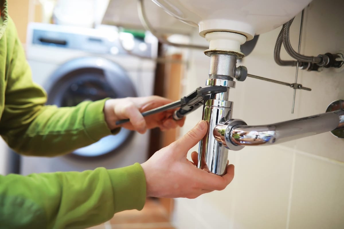 Septic System Summer Care in Woodstock: Preparing for Gatherings 6 A person uses a wrench to tighten or repair plumbing pipes under a sink, maintaining the system and ensuring everything—from the kitchen to the washing machine—runs smoothly with the home's septic system.