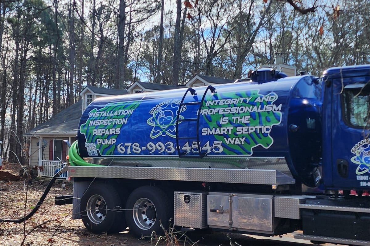 Septic System Inspection Process in Marietta, GA: What to Expect 2 A blue septic service truck with "Installation, Septic System Inspection, Repairs, Pump" and contact info is parked in front of a house nestled among trees.