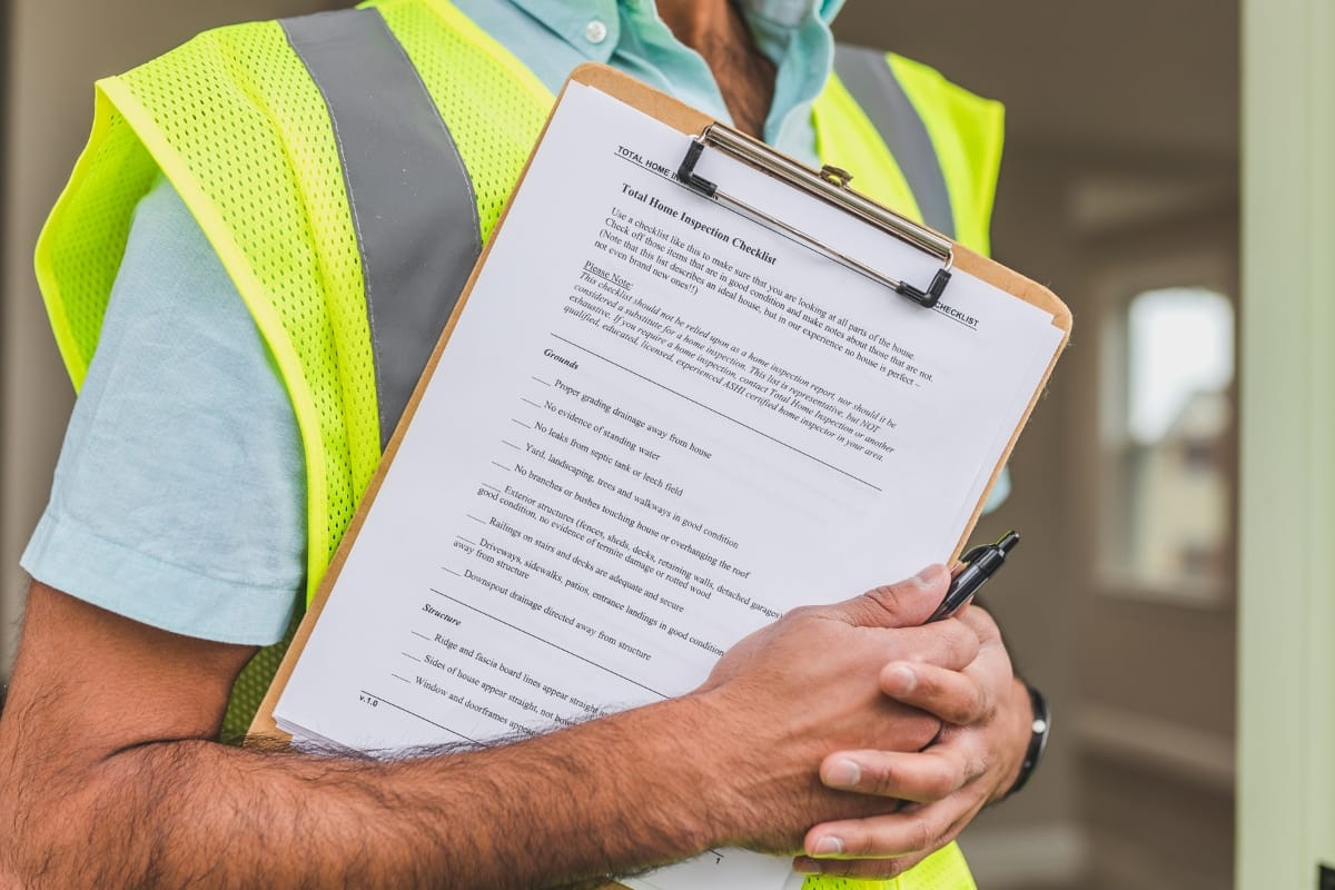 Septic System Inspection Process in Marietta, GA: What to Expect 8 Person in a yellow safety vest holds a clipboard with septic system inspection checklist paperwork and a pen, standing indoors.